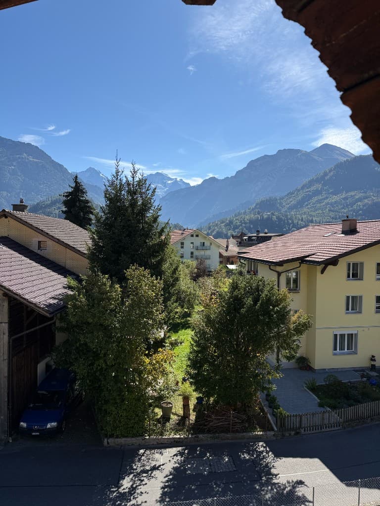 Aussicht aus einem Fenster im Obergeschoss auf Gärten und Berge
