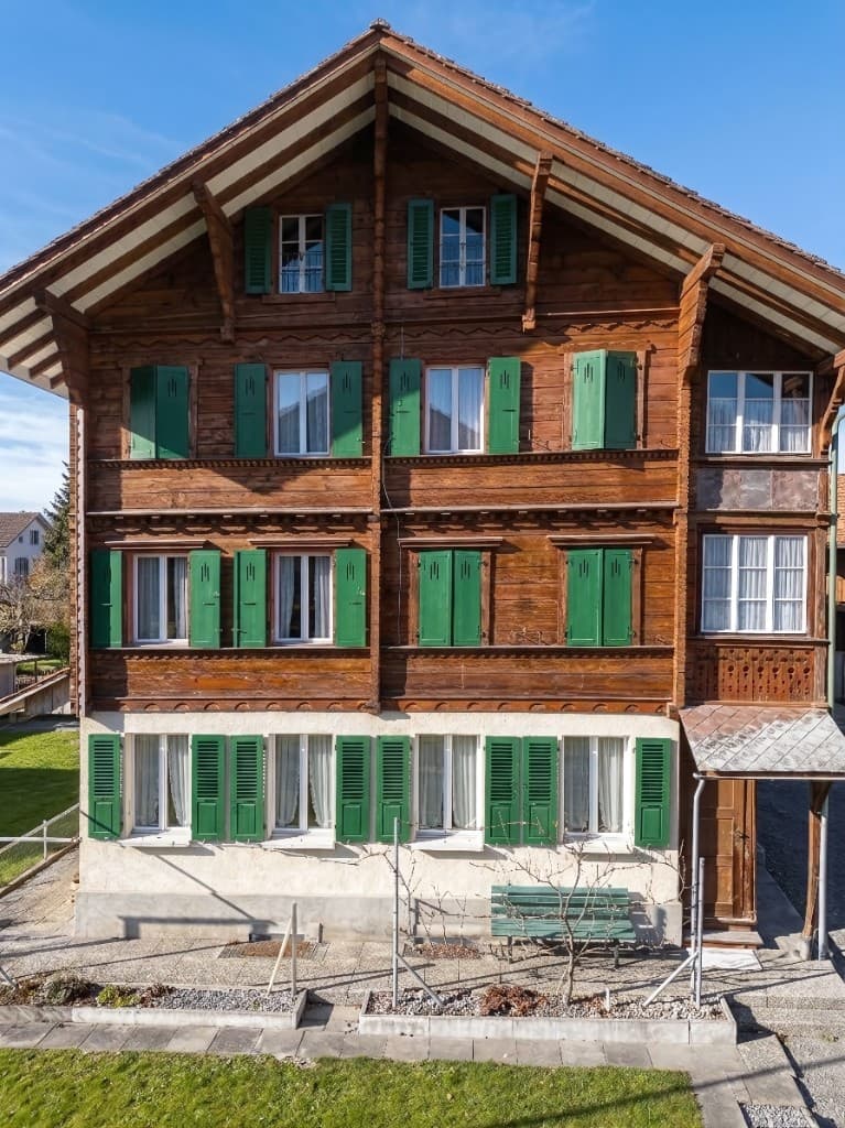 Frontalansicht der Holzfassade an der Freihofstrasse 18 mit Blockbau, grünen Fensterläden und geschnitztem Laubengang